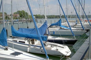 A marina with multiple sailboats docked, some with blue covers, and a calm water body in the background. - Holiday apartment with 1 bedroom (Lindau)