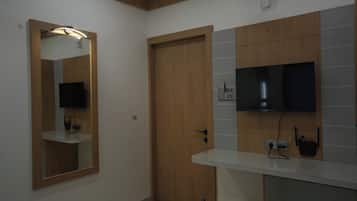 Een badkamer met een houten deur, een spiegel met verlichting, een flatscreen televisie en een witte wastafel.