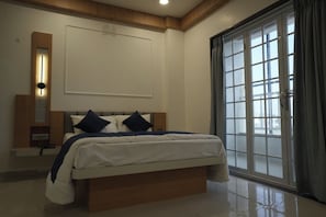 A bedroom with a large bed, a bedside table, a wall-mounted light, and a window with curtains. - Urban 24 Inn (Latur)