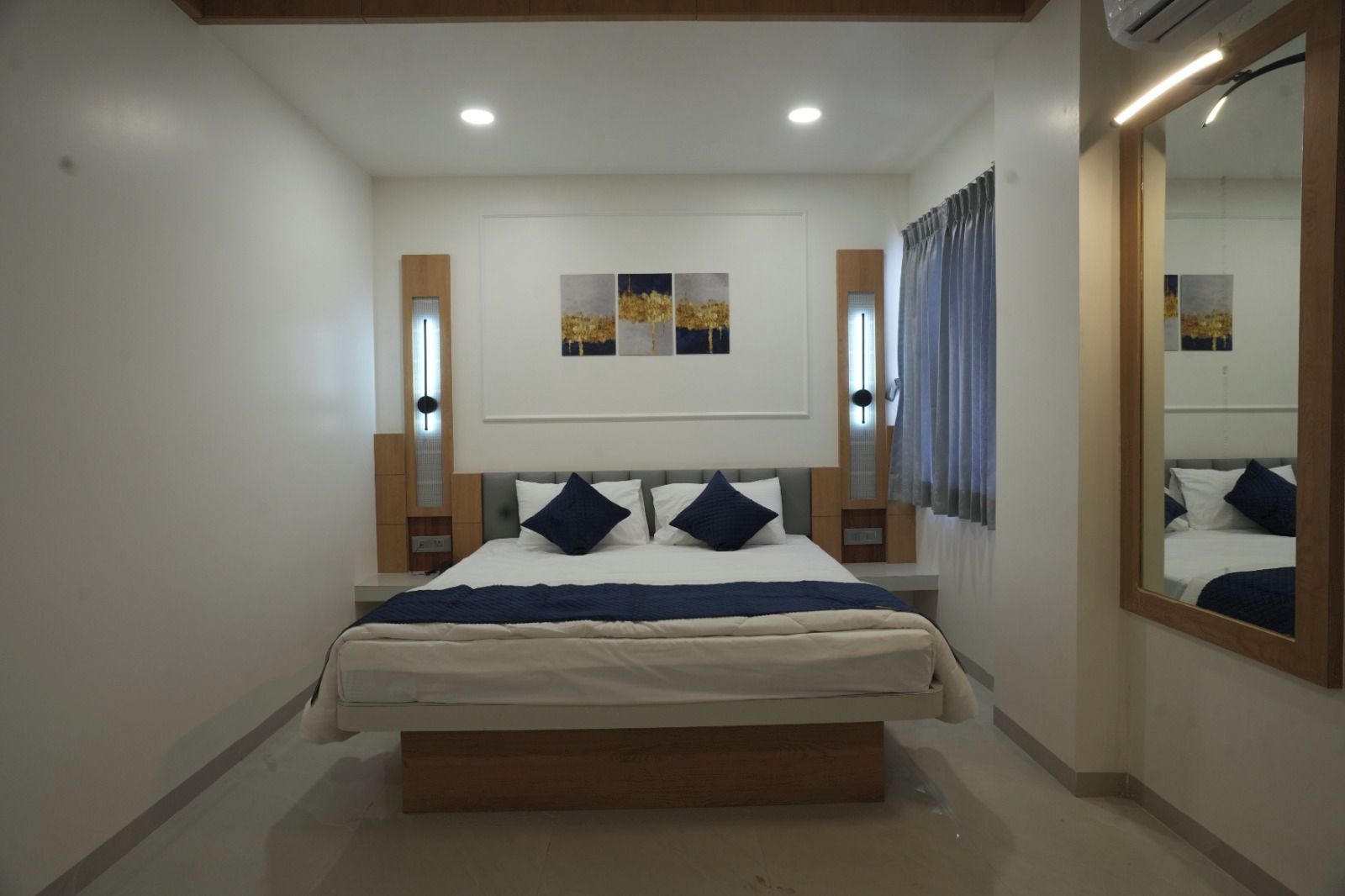 A bedroom with a bed, bedside tables, a mirror, and artwork on the wall.