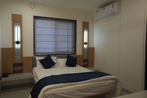 A bedroom with a bed, bedside tables, a window with blinds, and an air conditioning unit. - Urban 24 Inn (Latur)