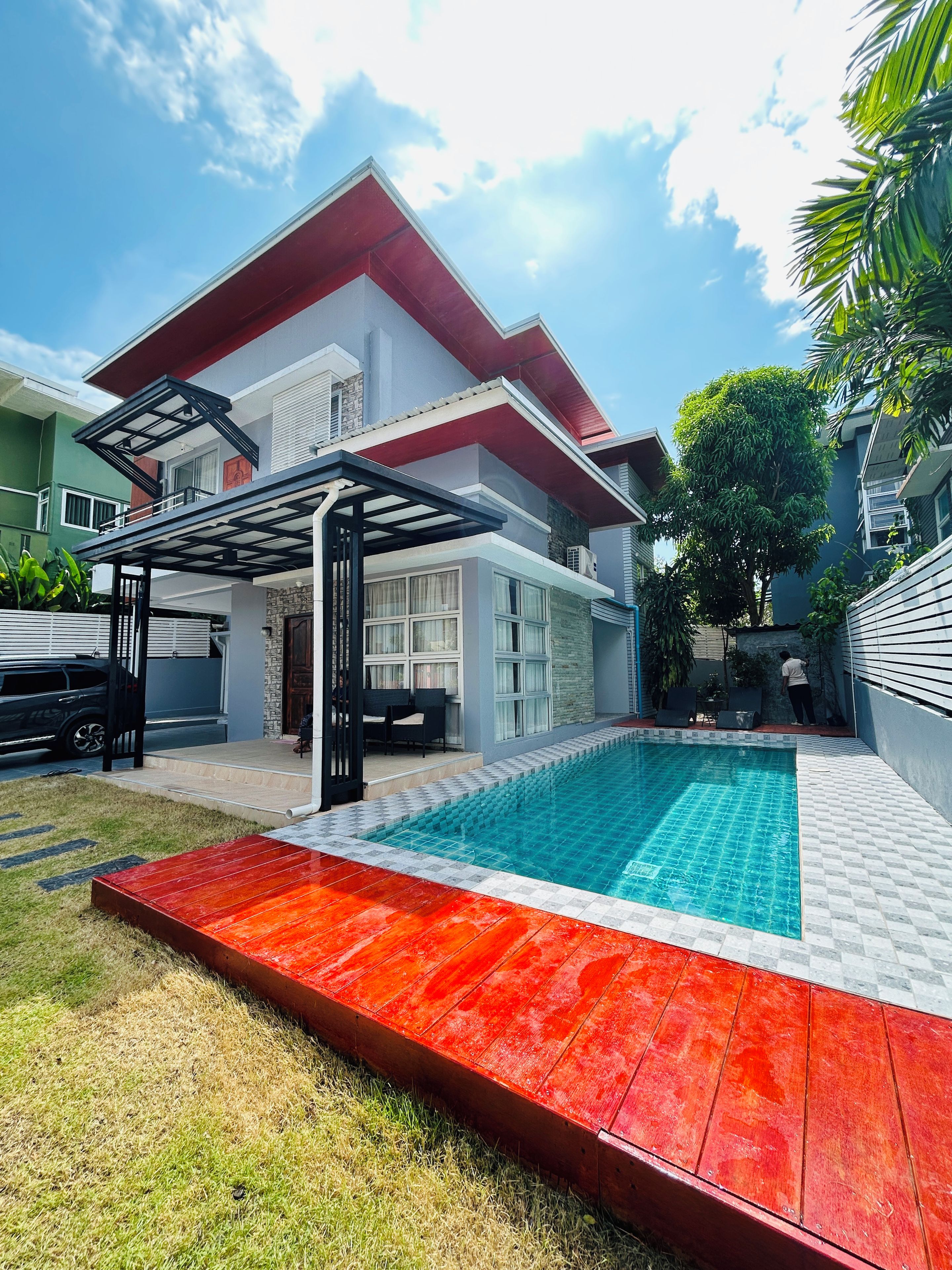 A modern house with a swimming pool, a covered patio, and a red deck.