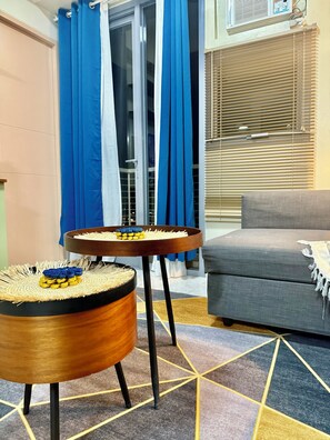 A room with a sofa, a round wooden table with a woven mat, and a window with blinds. - Boho Family Suite 3BR 2bath 2Balcony in St. Lukes QC Manila PH (Quezon City)