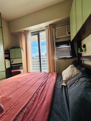 A hotel room with a bed, a window with curtains, an air conditioning unit, and a mirror. - Boho Family Suite 3BR 2bath 2Balcony in St. Lukes QC Manila PH (Quezon City)