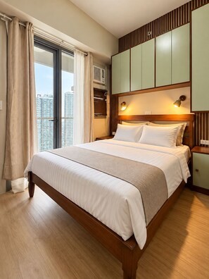 A hotel room with a large bed, a wardrobe, a nightstand, and a window with curtains.