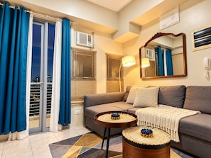 A modern living room with a sofa, two small side tables, a large mirror, and a view of the city through a sliding glass door.