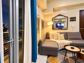 A modern living room with a sofa, a television, a lamp, and a view of the city at night. - Boho Family Suite 3BR 2bath 2Balcony in St. Lukes QC Manila PH (Quezon City)