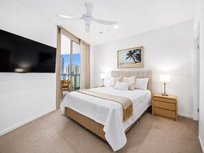 Una camera d'albergo con un letto, comodini, una ventola a soffitto, una finestra che dà su edifici e un quadro appeso al muro.