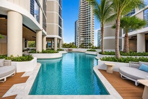 A swimming pool with a curved design, surrounded by white planters and palm trees. - Coastal Retreat at Lagoon Main Beach (Main Beach)