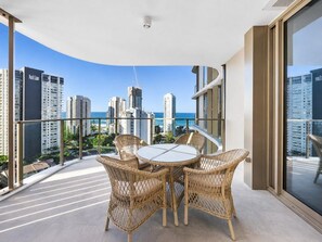 A balcony with a round table and wicker chairs, overlooking a cityscape with high-rise buildings and a clear sky. - Coastal Retreat at Lagoon Main Beach (Main Beach)