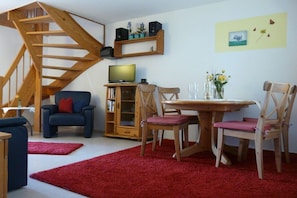 A living room with a wooden staircase, a television, a dining table with chairs, and a bookshelf. - Holiday apartment with 2 bedrooms (Langenargen)