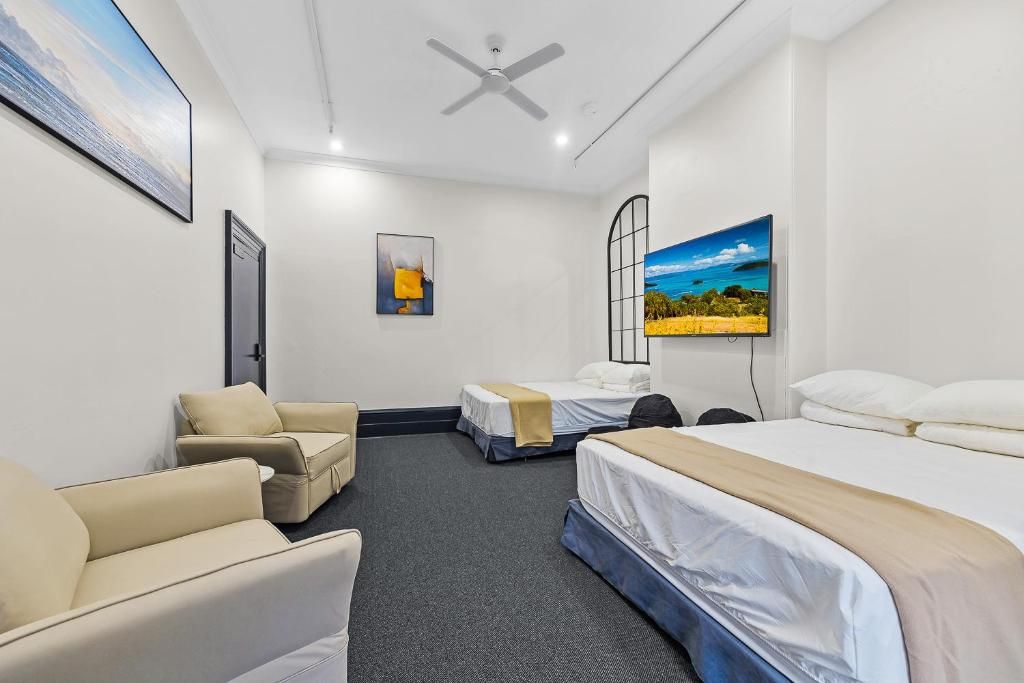A hotel room with a bed, two single beds, a sofa, a desk, and a television.