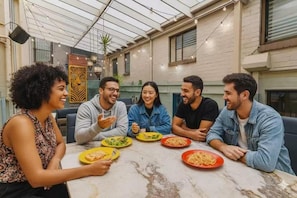 A group of people dining at a table with various dishes in a room with a high ceiling and brick walls. - London Gate Backpackers Hostel (Potts Point)