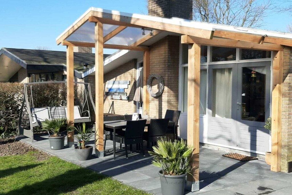 Un patio couvert comprenant une table et des chaises, des plantes en pot et une structure en forme de pergola en bois.