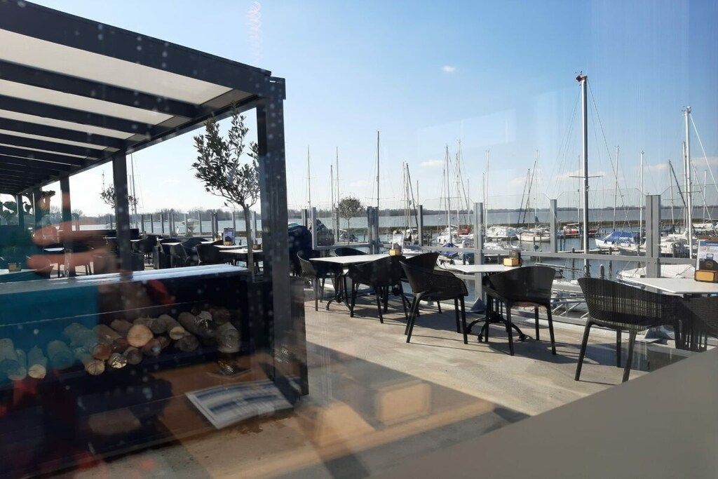 An outdoor seating area with tables and chairs, overlooking a marina with boats.