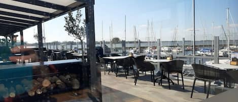An outdoor seating area with tables and chairs, overlooking a marina with boats.