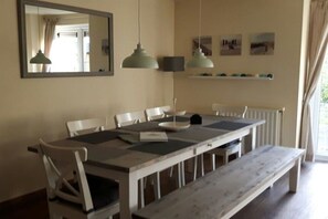 Un espace repas comprenant une table, des chaises, un banc, un miroir, des luminaires suspendus et des étagères fixées au mur.