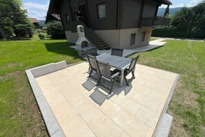 A patio with a table and chairs, a barbecue grill, and a house in the background. - Feldblick 44th floor (Arrach)