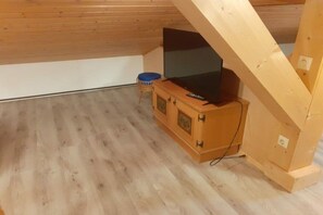 A room with a sloped ceiling, a television on a wooden cabinet, and a small stool. - Feldblick 44th floor (Arrach)