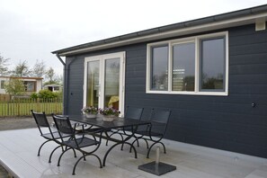 A patio with a table and chairs, a covered area, and a dark building with windows. - Cabin in Schagen with swimming pool (Schagen)