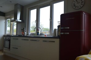 A kitchen with a red refrigerator, a stove, a sink, and a window with a view. - Cabin in Schagen with swimming pool (Schagen)