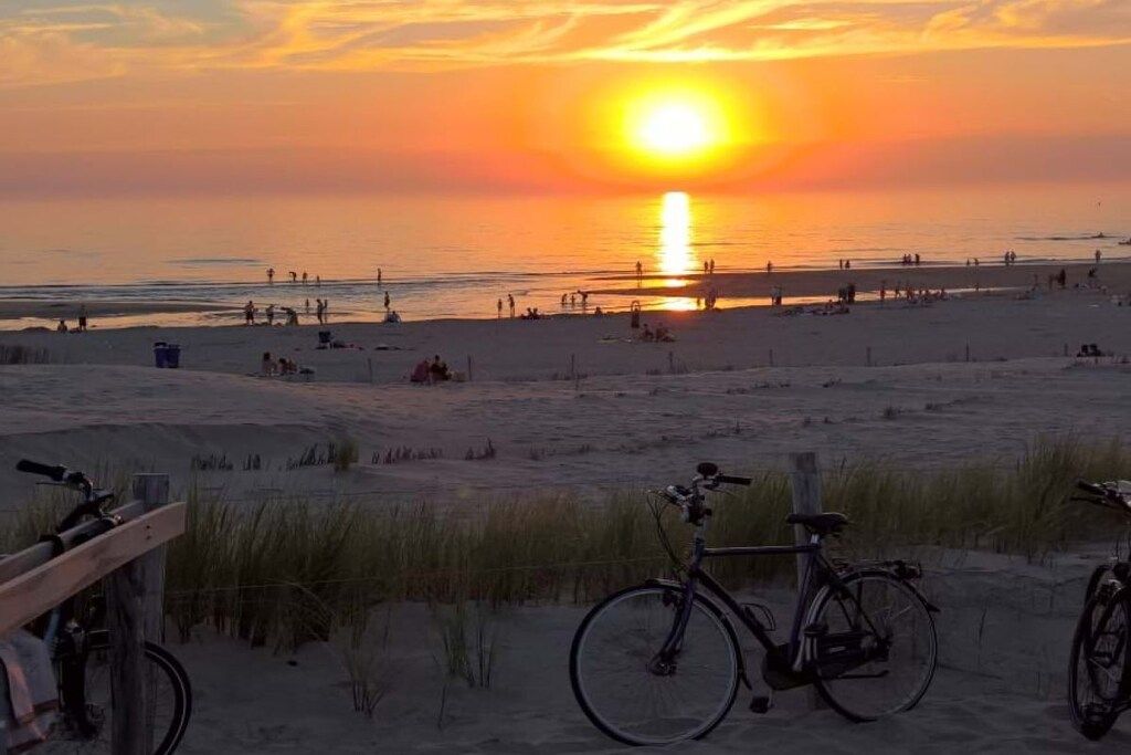 Eine Strandansicht mit einem am Sand abgestellten Fahrrad, einem Holzzaun und einem klaren Himmel.