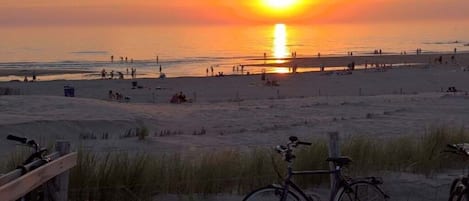 Escena de platja amb una bicicleta aparcada a la sorra, una tanca de fusta i un cel serè.