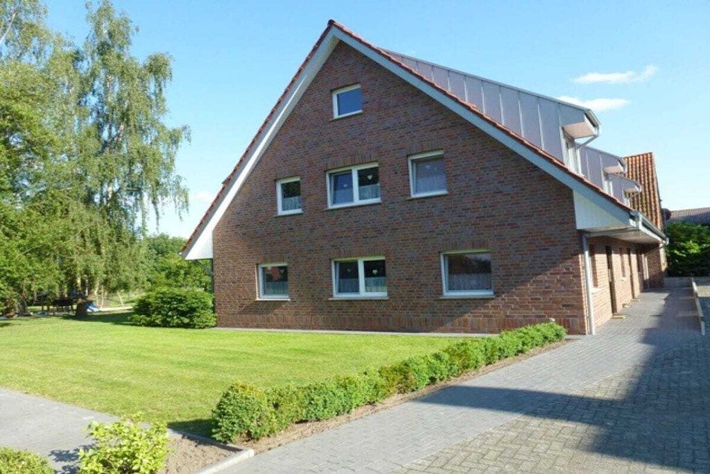 Ein zweistöckiges Backsteinhaus mit geneigtem Dach und mehreren Fenstern, mit einer gepflasterten Auffahrt.