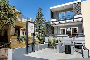 A modern building with a balcony, a sign for 'Sol Apartments,' and a tree in the foreground. - Amara Solar Living Partial Sea View Apartment (Agia Marina)