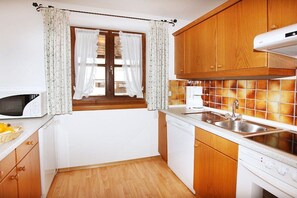 A compact kitchen with wooden cabinets, a microwave, a dishwasher, and a tiled backsplash. - Holiday apartment with 2 bedrooms (Wallgau)