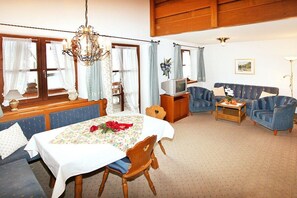 A cozy living room with a dining table, blue sofas, a television, and a chandelier. - Holiday apartment with 2 bedrooms (Wallgau)
