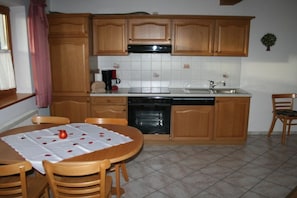 A kitchen with wooden cabinets, a stove, a sink, and a dining table set with a tablecloth and a red apple. - Holiday apartment with 2 bedrooms (Samerberg)