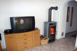 A television on a wooden cabinet, a fireplace with a visible fire, and a wicker basket on the floor. - Holiday apartment with 2 bedrooms (Samerberg)