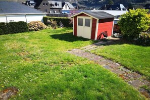 A red shed in a grassy yard with a stone path leading to it, surrounded by houses and a mountain in the background. - Apartment with balcony overlooking the castle (Bernkastel-Kues)