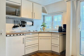 A compact kitchen with white cabinets, a microwave, and a variety of utensils hanging above the counter. - Holiday apartment with 1 bedroom (Nonnenhorn)