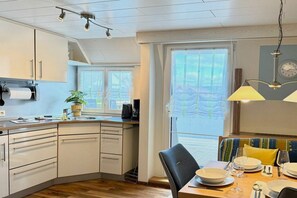 A modern kitchen with a dining area, featuring a built-in oven, a sink, and a window with curtains. - Holiday apartment with 1 bedroom (Nonnenhorn)