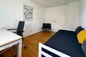 A room with a bed, a desk, a chair, and a door. - Holiday apartment with 1 bedroom (Wasserburg)