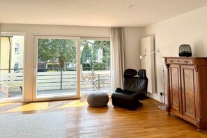 Ein Zimmer mit Holzboden, einem schwarzen Ledersessel, einem grauen Hocker und einem Holzkabinett.