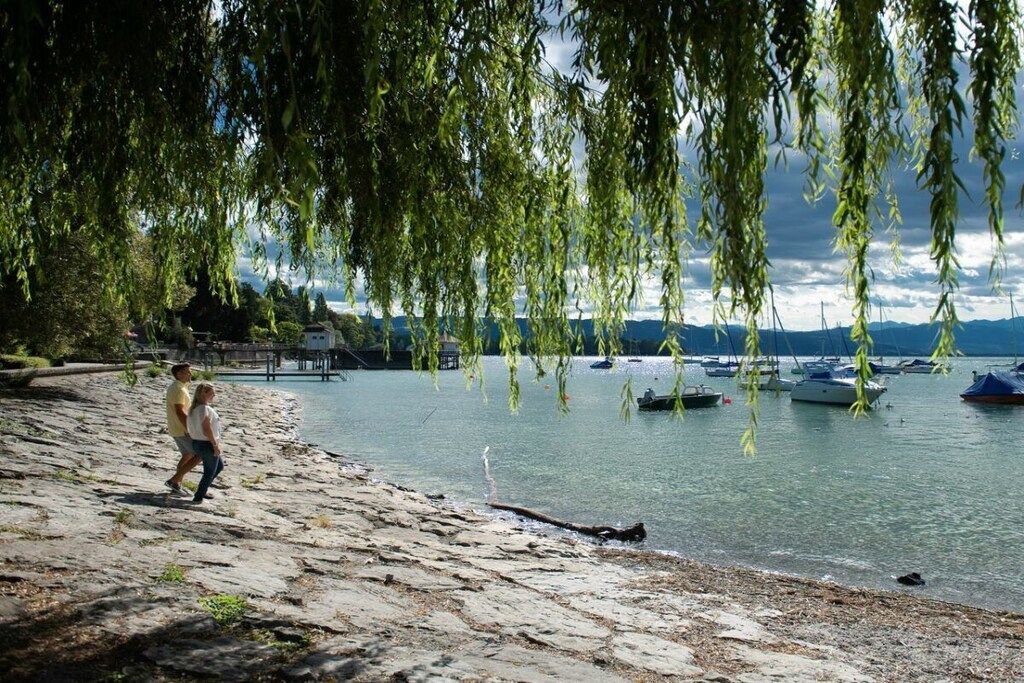 Een rotsachtige kustlijn met water, boten en een persoon die loopt.