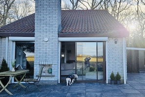 Une maison moderne avec une façade en briques, un toit en tuiles et une porte vitrée donnant sur un patio.