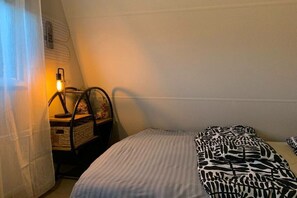 A bedroom with a bed, a nightstand, a lamp, and a window. - Forest cottage by the sea (Sint Maartensvlotbrug)