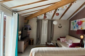 Quarto aconchegante com cama, sofá, televisão e escrivaninha. Cortinas e um quadro adornam a parede.