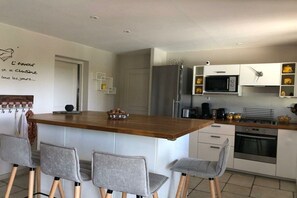 A modern kitchen with a central island, bar stools, a microwave, refrigerator, and an oven. - gîte in St-Sauveur-de-Cruzières (Commune)