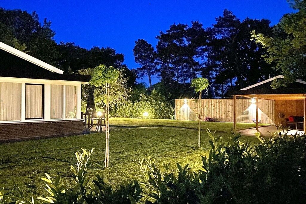 A well-lit backyard with a wooden fence, a lawn, and a building with large windows.