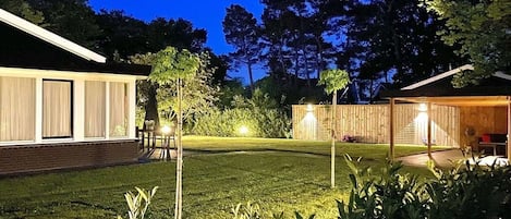 Quintal bem iluminado, com cerca de madeira, gramado e um edifício com grandes janelas.