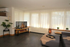 Una sala de estar con un televisor de pantalla plana, un sofá, una mesa de centro y una lámpara de pie.