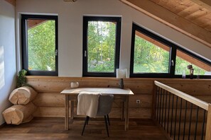 A room with a wooden desk, two windows with black frames, and a view of greenery outside. - Cabin in Spiegelau with swimming pool (Spiegelau)