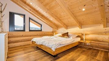 Ein Schlafzimmer mit Holzwänden, einem Bett, zwei Fenstern und Blick ins Freie.