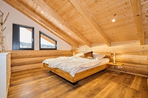 A wooden-paneled bedroom with a bed, two windows, and a view of the outdoors. - Cabin in Spiegelau with swimming pool (Spiegelau)