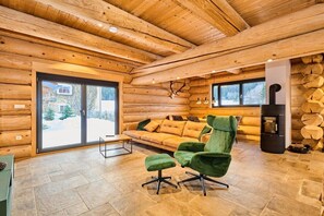 A log cabin interior with a sofa, green armchair, and a fireplace.